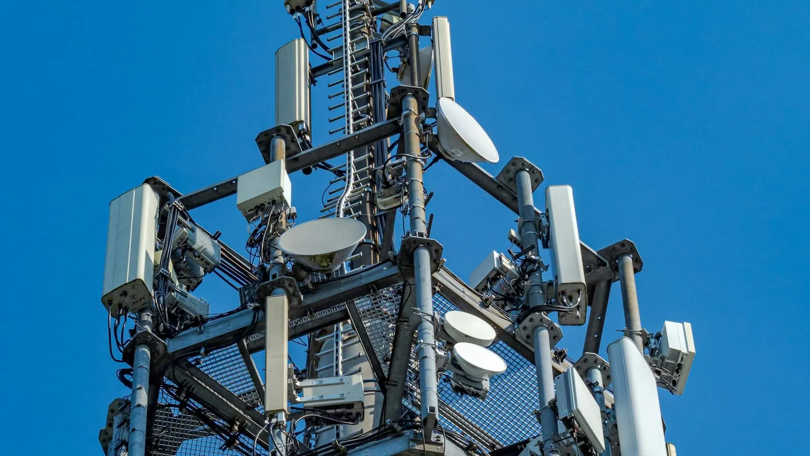 A cell tower with antennas and dishes against a blue sky